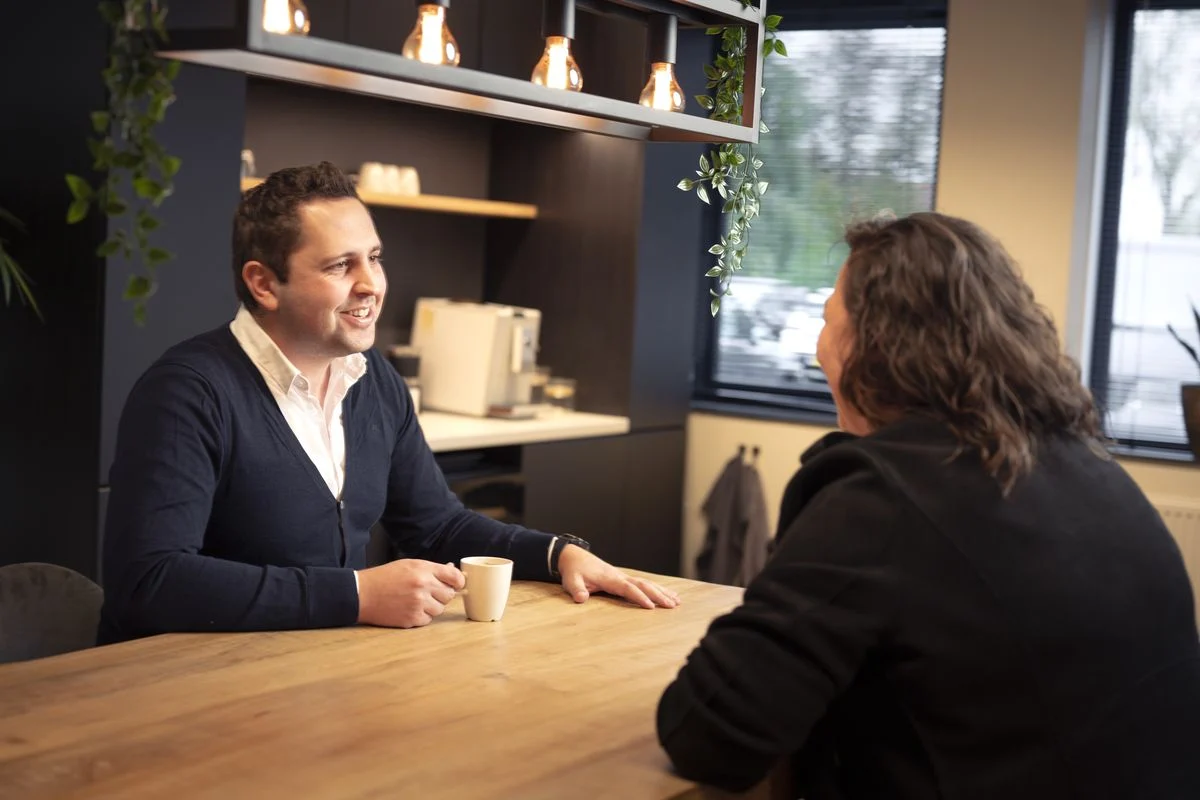 Twee collega's in gesprek aan tafel met een kop koffie